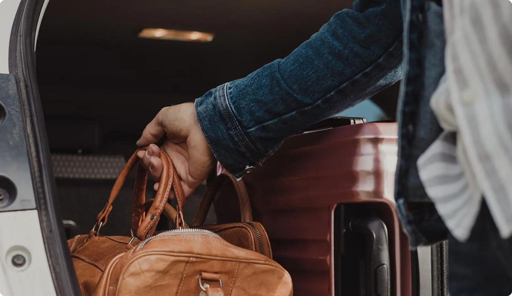 Ruka človeka vkladá koženú tašku do kufra auta vedľa cestovného kufra.